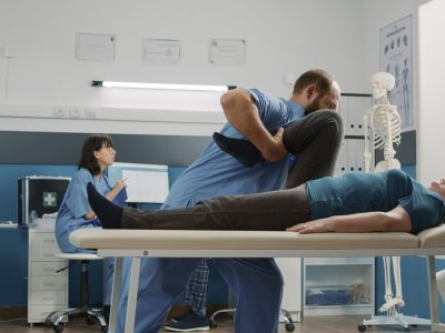 Orthopedic specialist and elder woman stretching arms and legs muscles at physical therapy appointment. Physiotherapist using alternative medicine procedure to increase mobility.